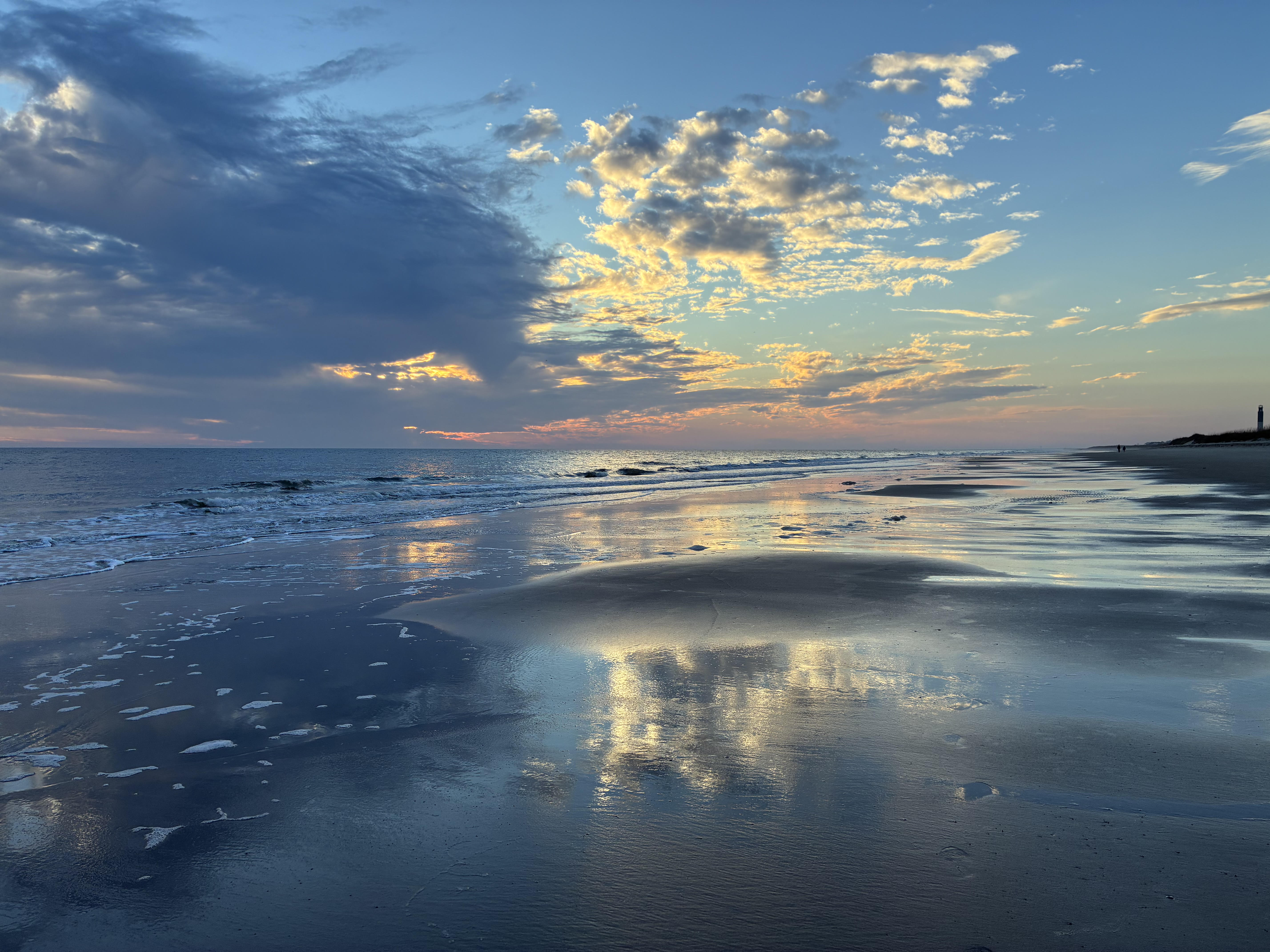 Sunset over a beach with reflective water and clouds.
